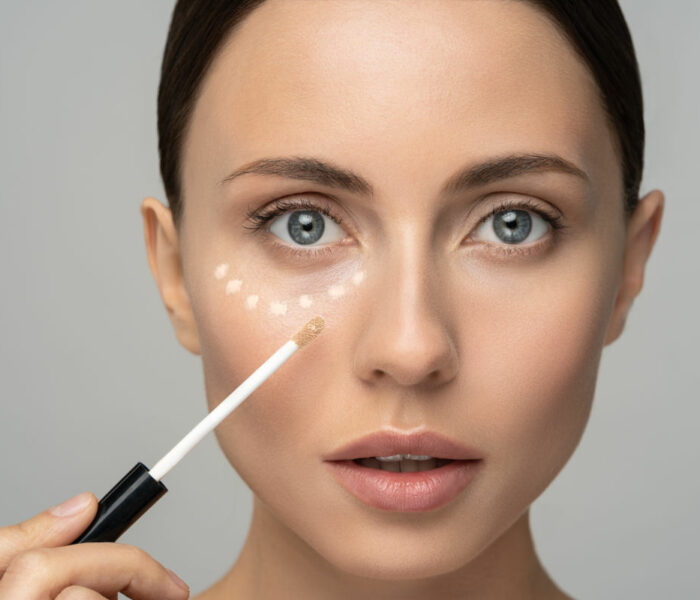 Close up of woman with natural makeup applying corrector on flawless fresh skin, doing make up. Girl after shower put concealer under eye area. Beauty face, skin care. Copy space, banner, advertising.